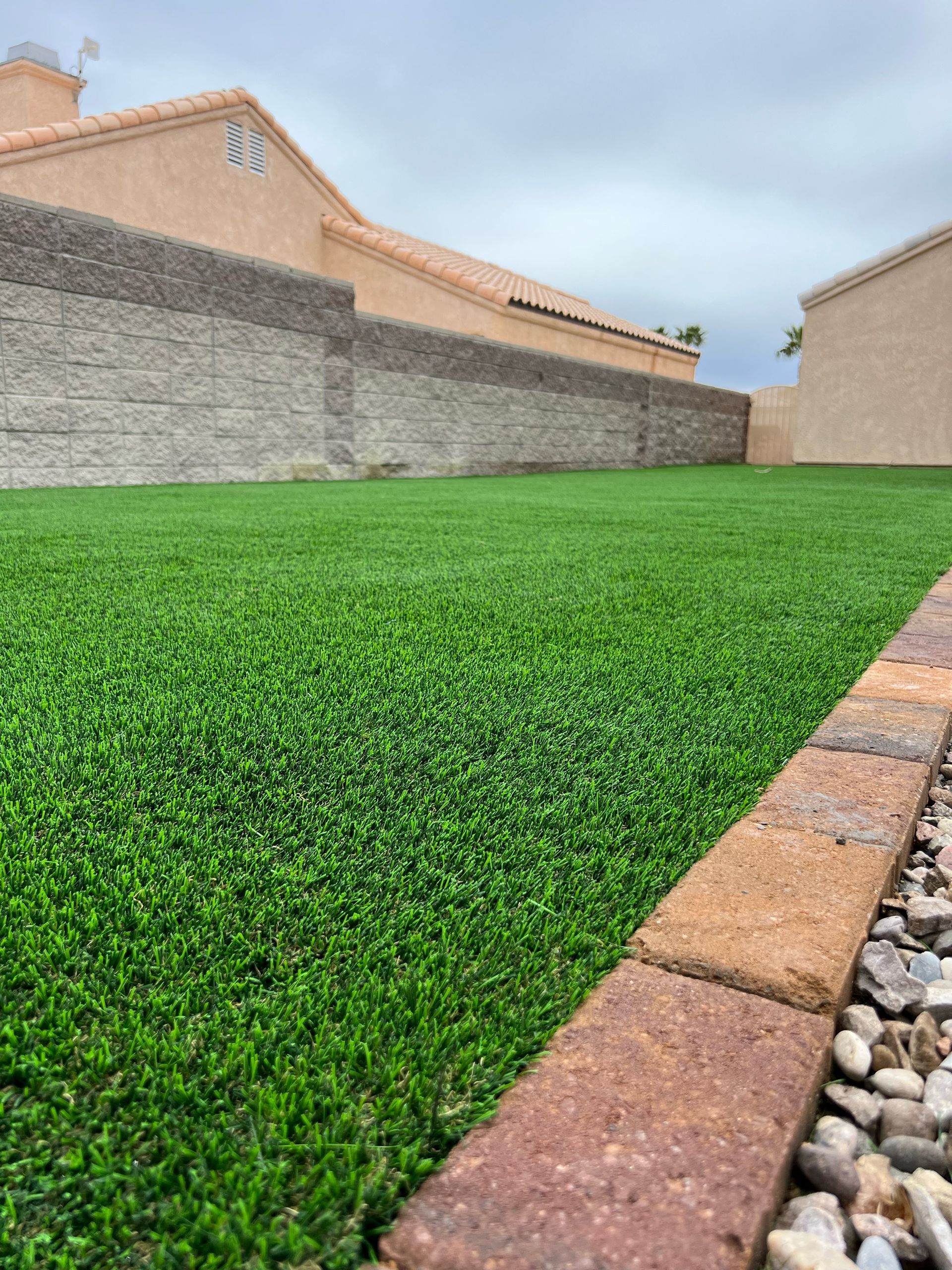 A lawn with a brick border and a brick wall in the background.