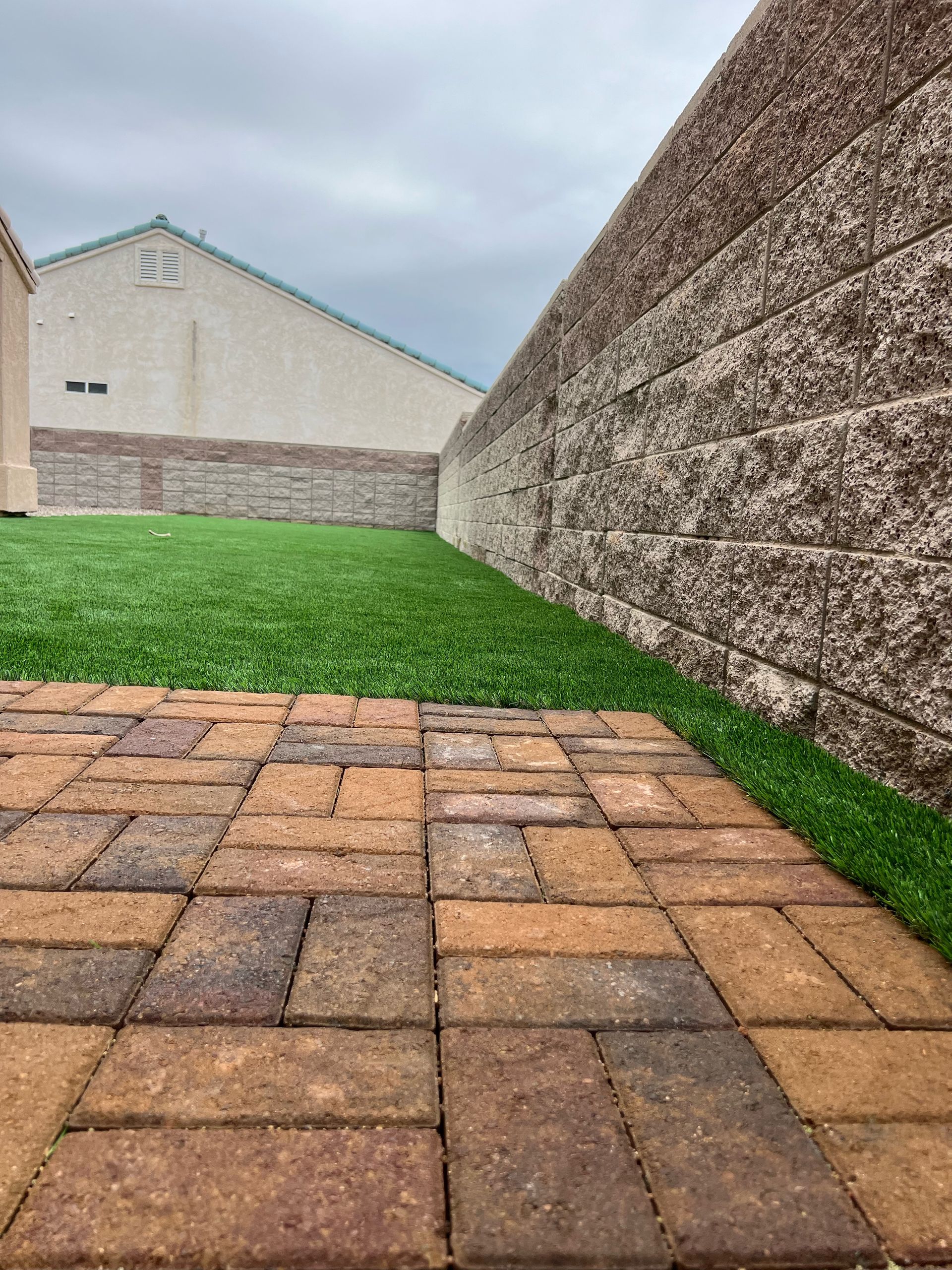 A brick walkway leading to a lush green lawn next to a stone wall.