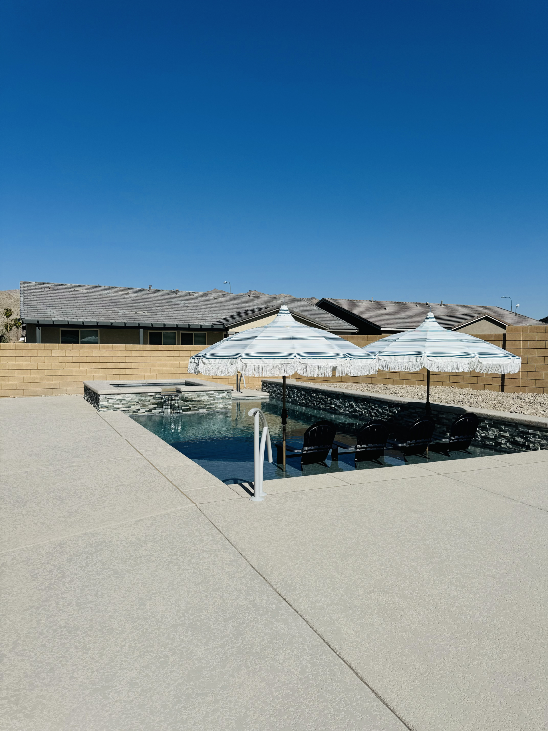 A swimming pool with umbrellas and chairs in front of a house.