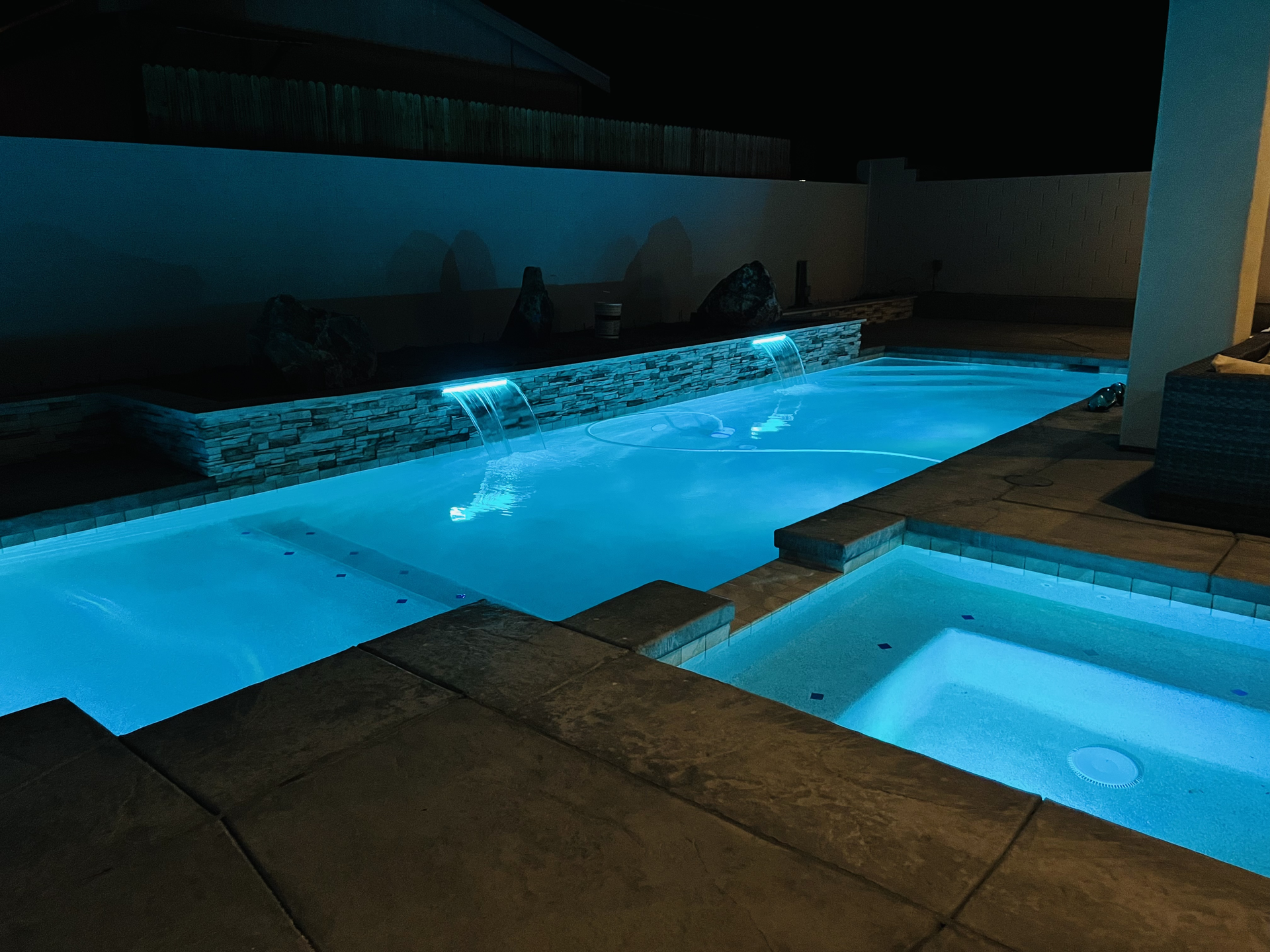A large swimming pool and hot tub are lit up at night.