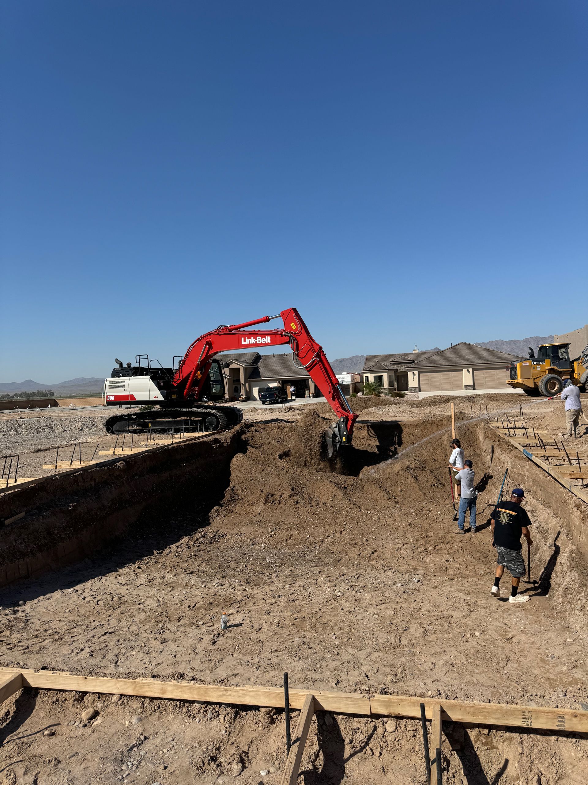 A red excavator is digging a hole in the dirt on a construction site.