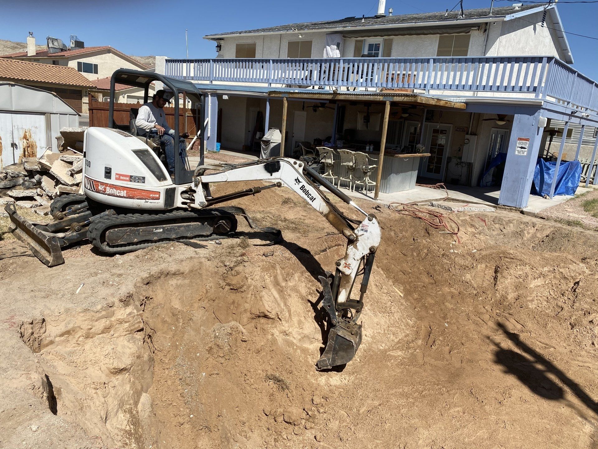 A man is driving an excavator in front of a house.