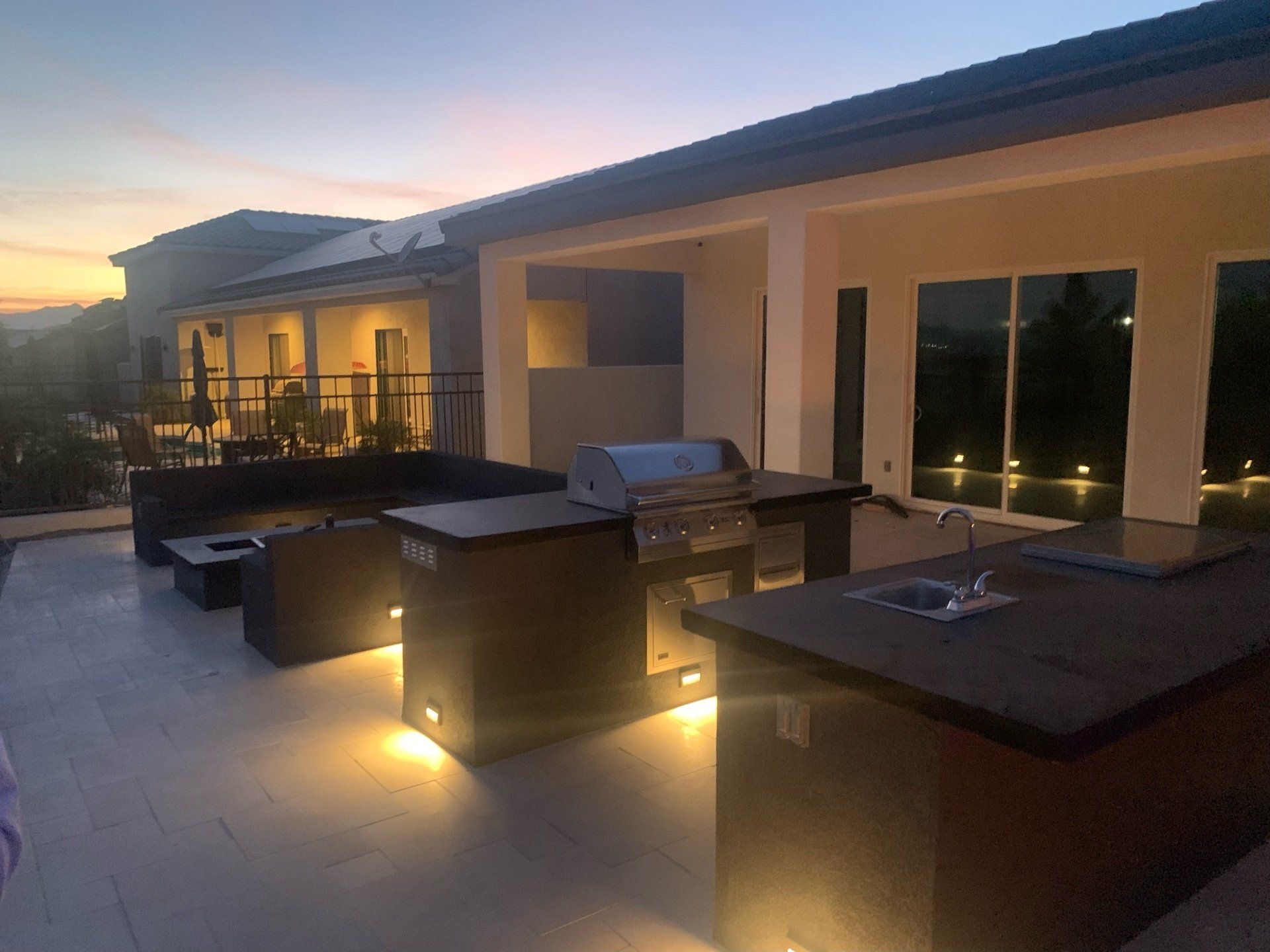 A patio with a grill and a sink in front of a house at night.