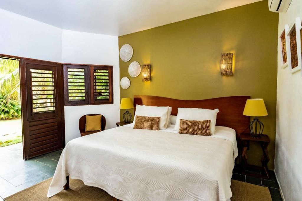 Quarto com cama king size, parede verde-oliva, portas duplas abertas e detalhes decorativos.