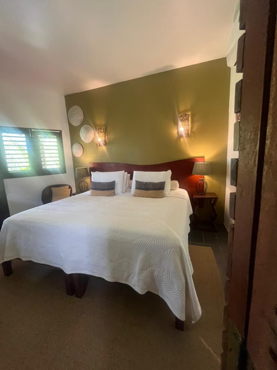 Quarto com uma cama, parede verde, duas arandelas e pratos decorativos.