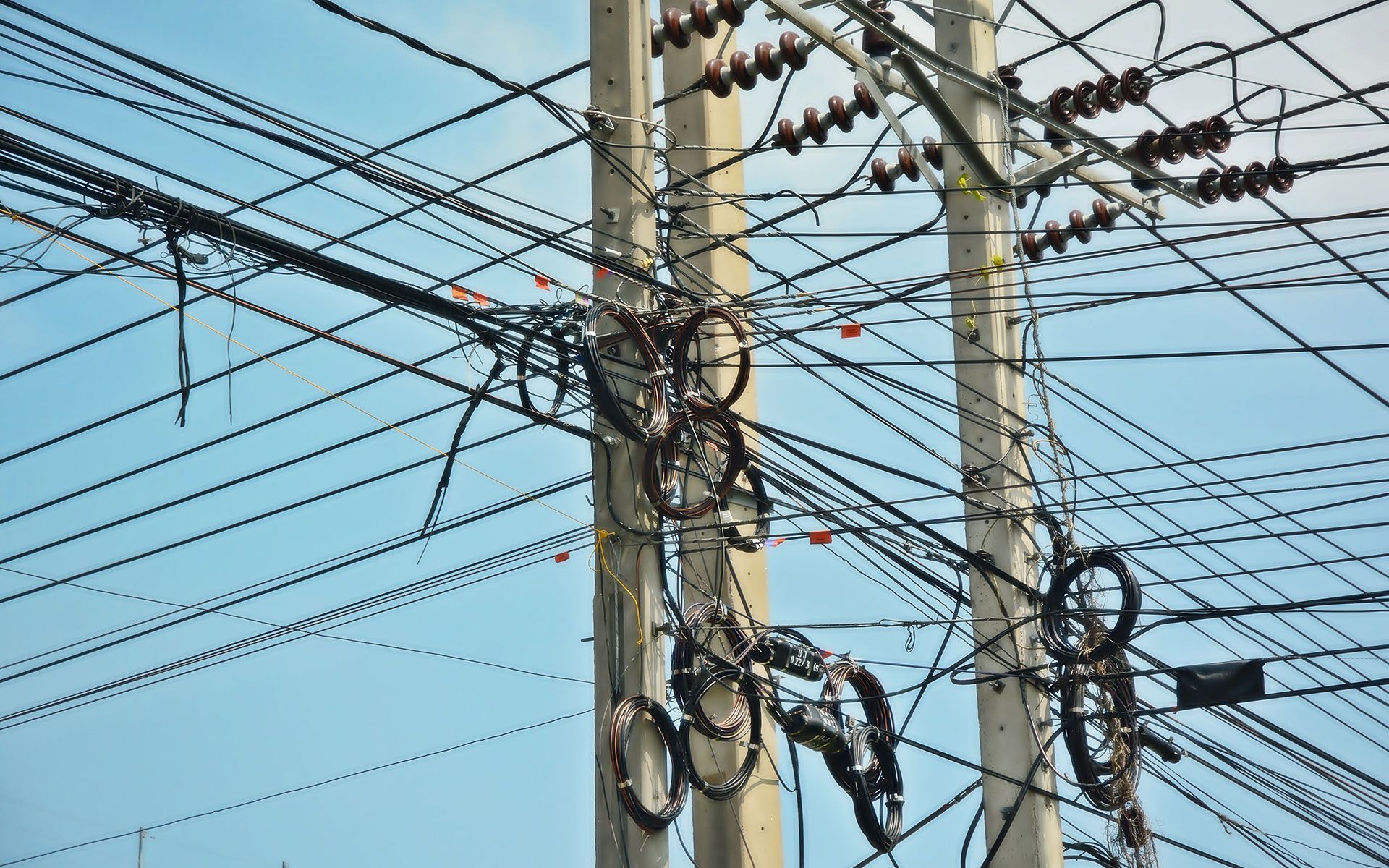 Overhead view of utility poles with tangled power lines against a blue sky.