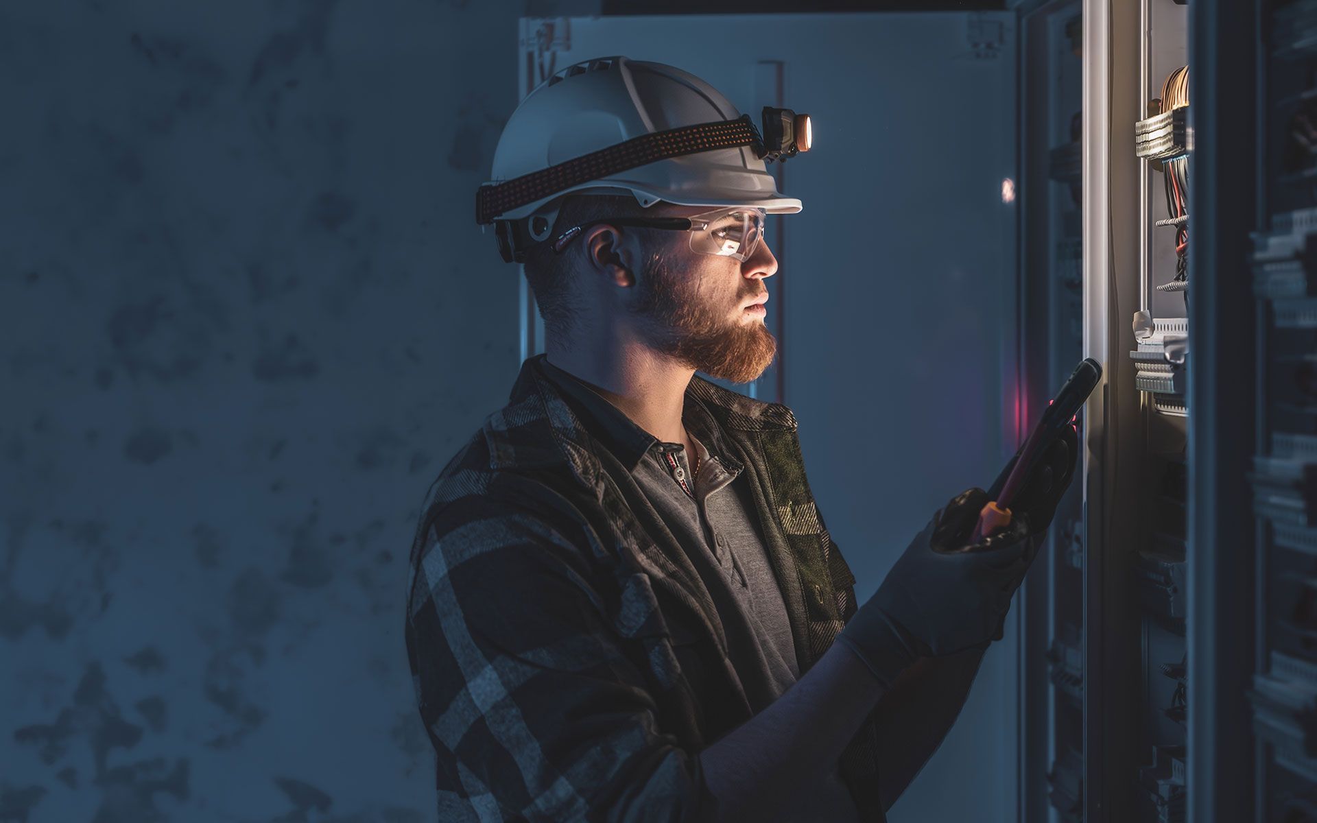 Electrician with headlamp inspecting electrical panel.