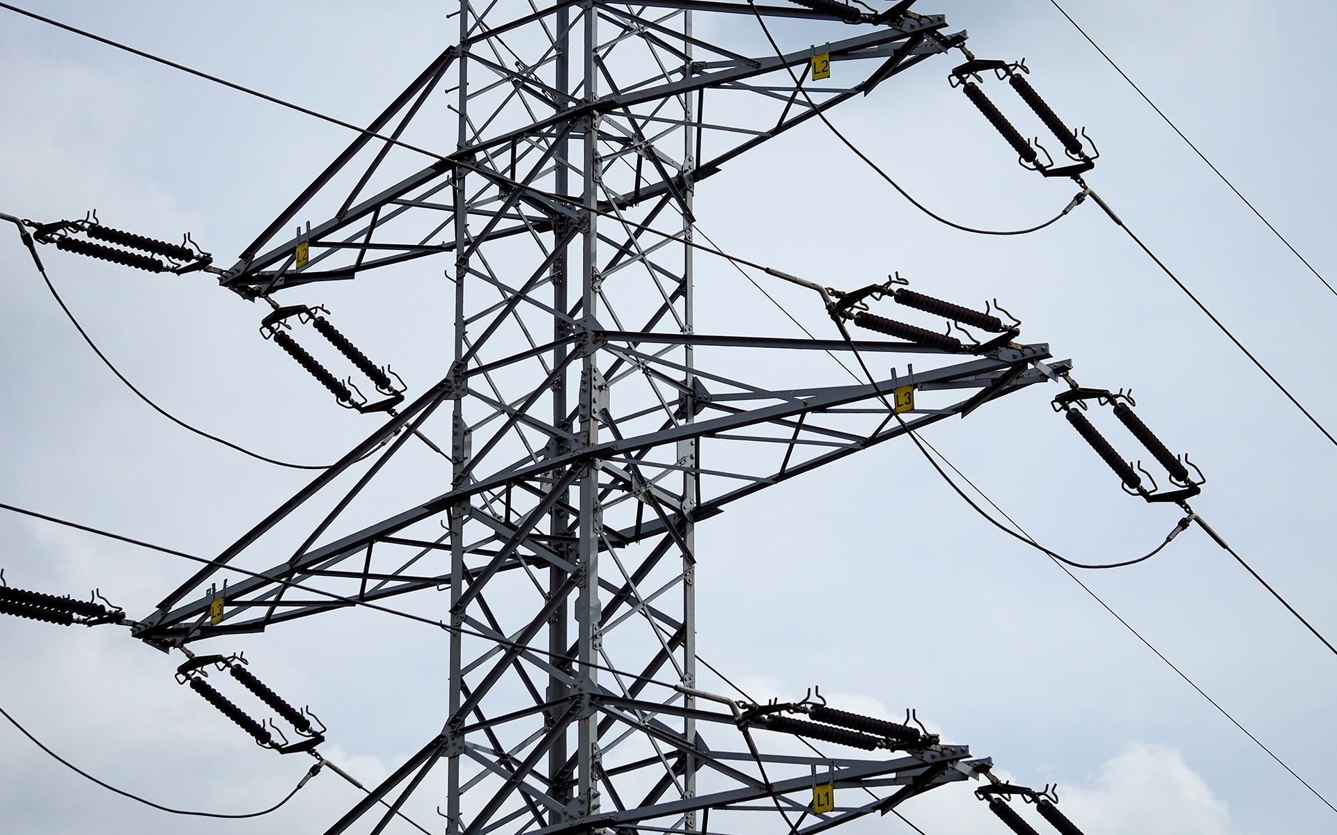 Metal electricity pylon, wires, and insulators against a cloudy sky.