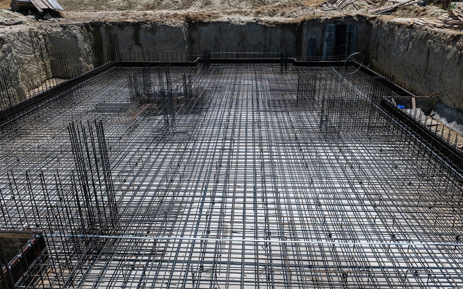 Reinforced steel grid within a rectangular foundation pit, prepared for concrete pouring.