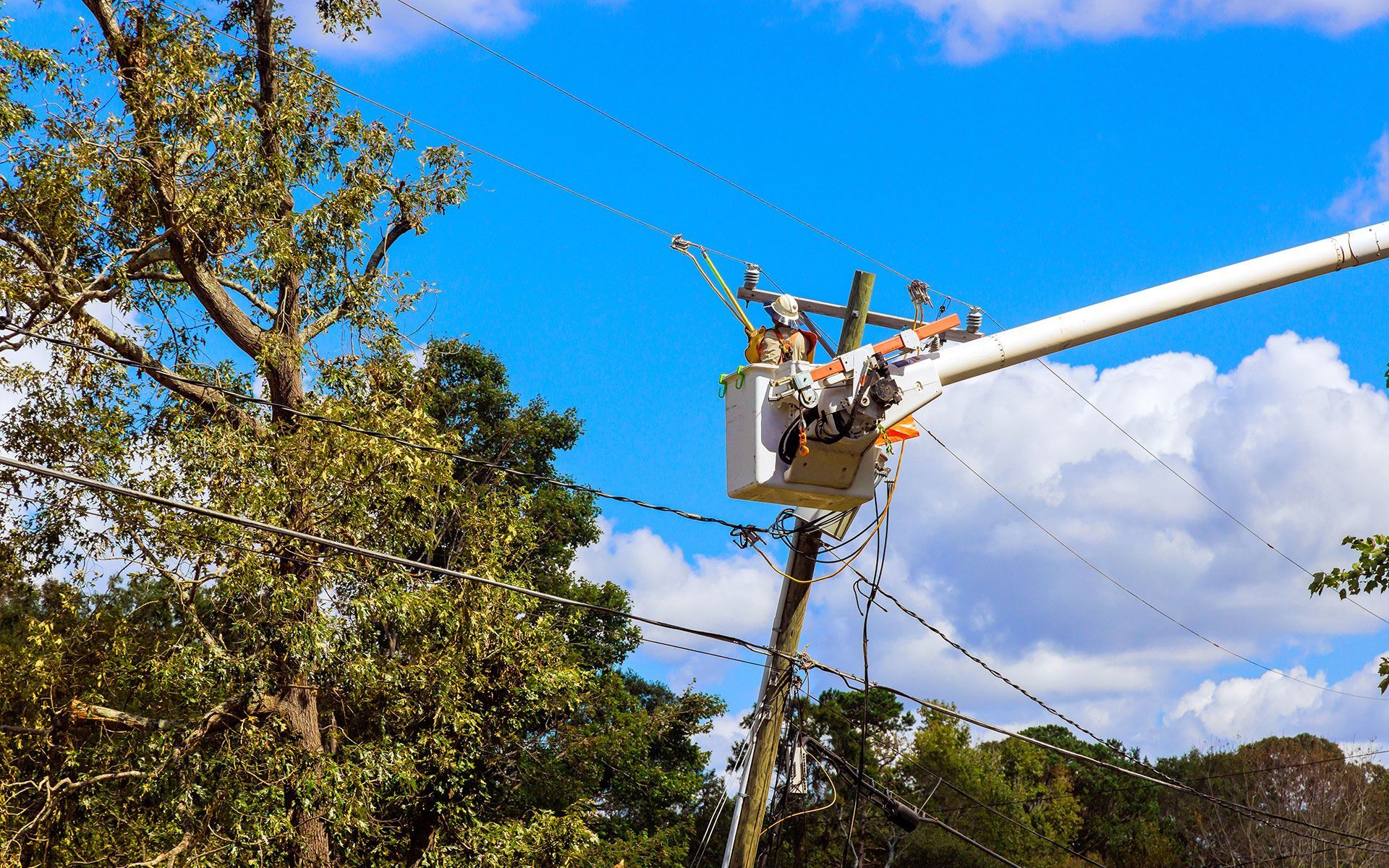 Linemen working on power lines in a bucket truck, repairing utility lines under a blue sky.