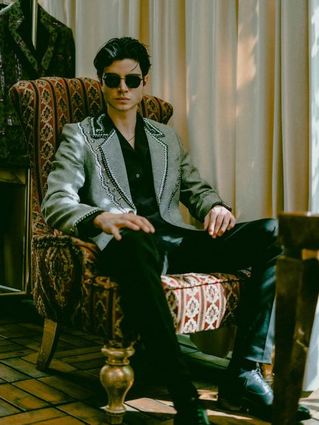 A man in a suit and sunglasses is sitting in a chair.