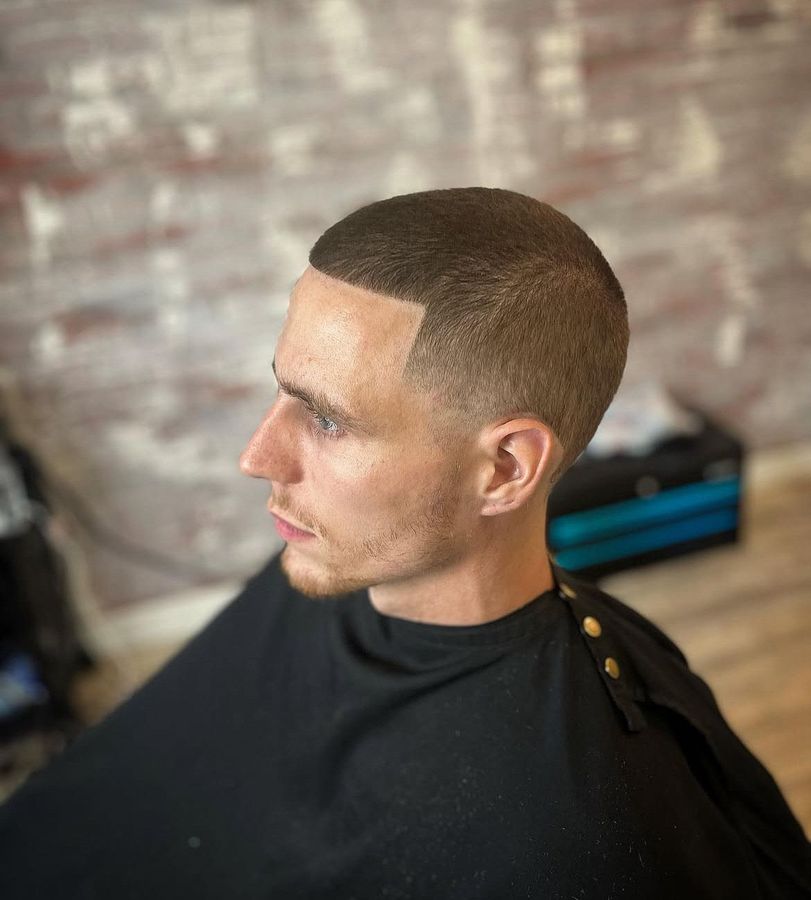 Red barber chair in a barbershop with mirrors, sink, and various products. Patterned floor.
