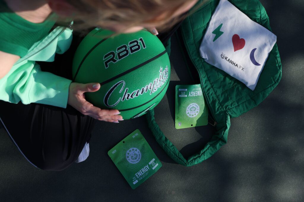 Woman holding a green basketball and a matching tote bag with energy drink packets on the ground.