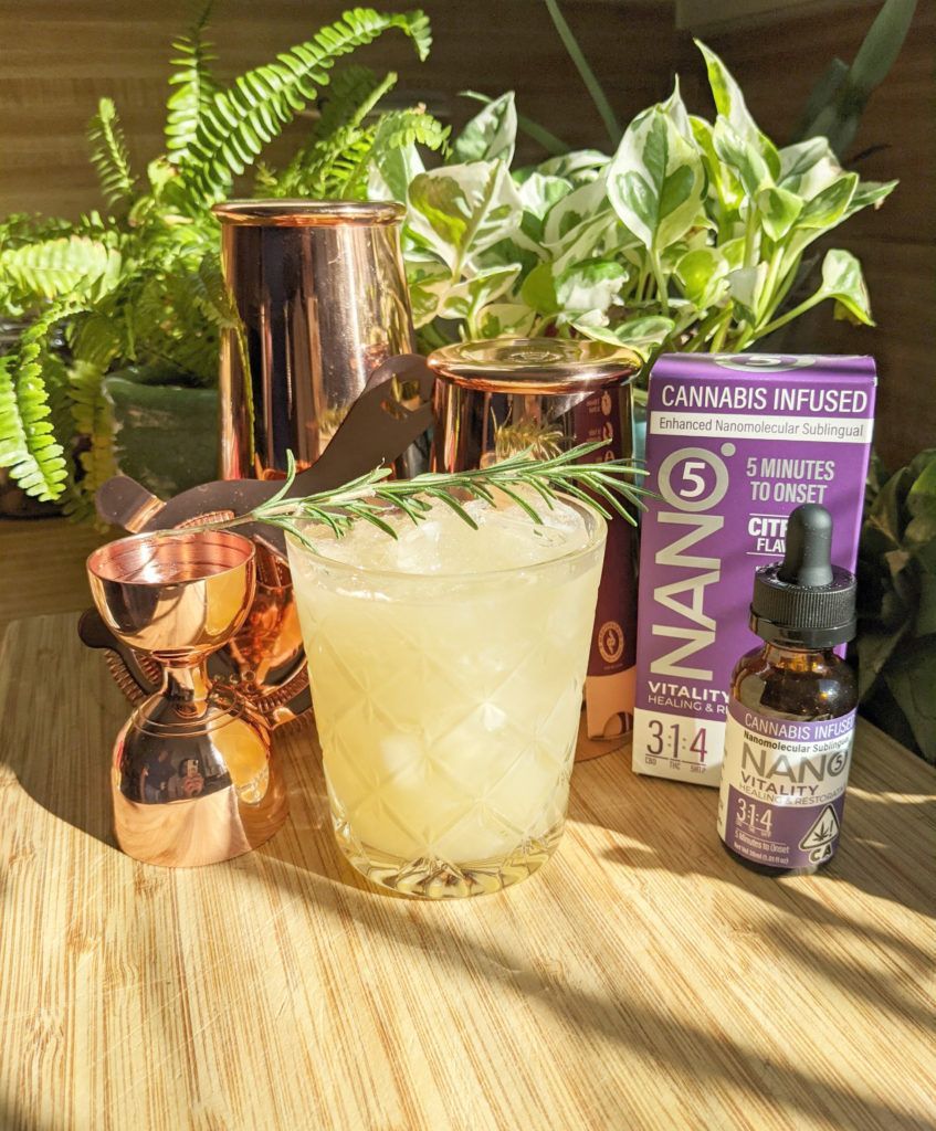 Cocktail with ice, rosemary sprig, copper bar tools, and cannabis-infused drops. Plants and wooden surface.