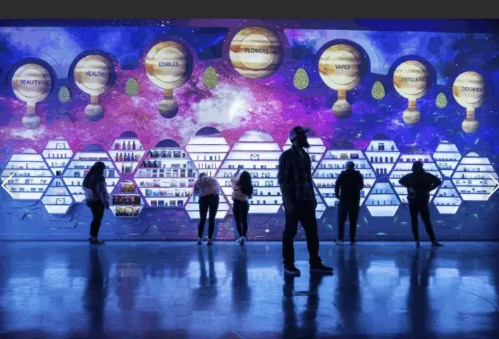 People viewing a display with illuminated hexagonal shelves holding products and a cosmic-themed background with planets.