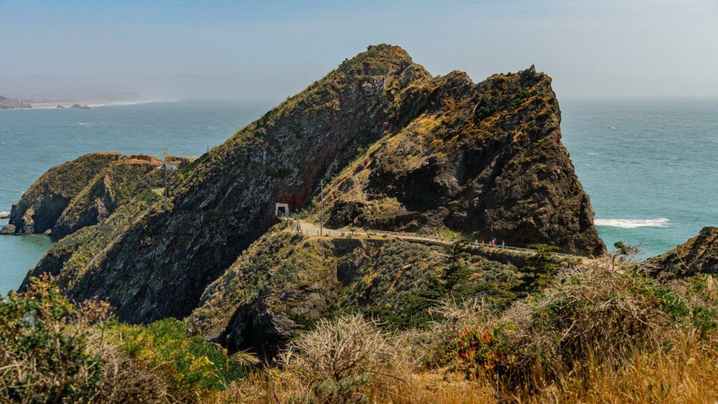 Rocky coastal landscape with a path winding across the terrain. Blue ocean and sky in the background.