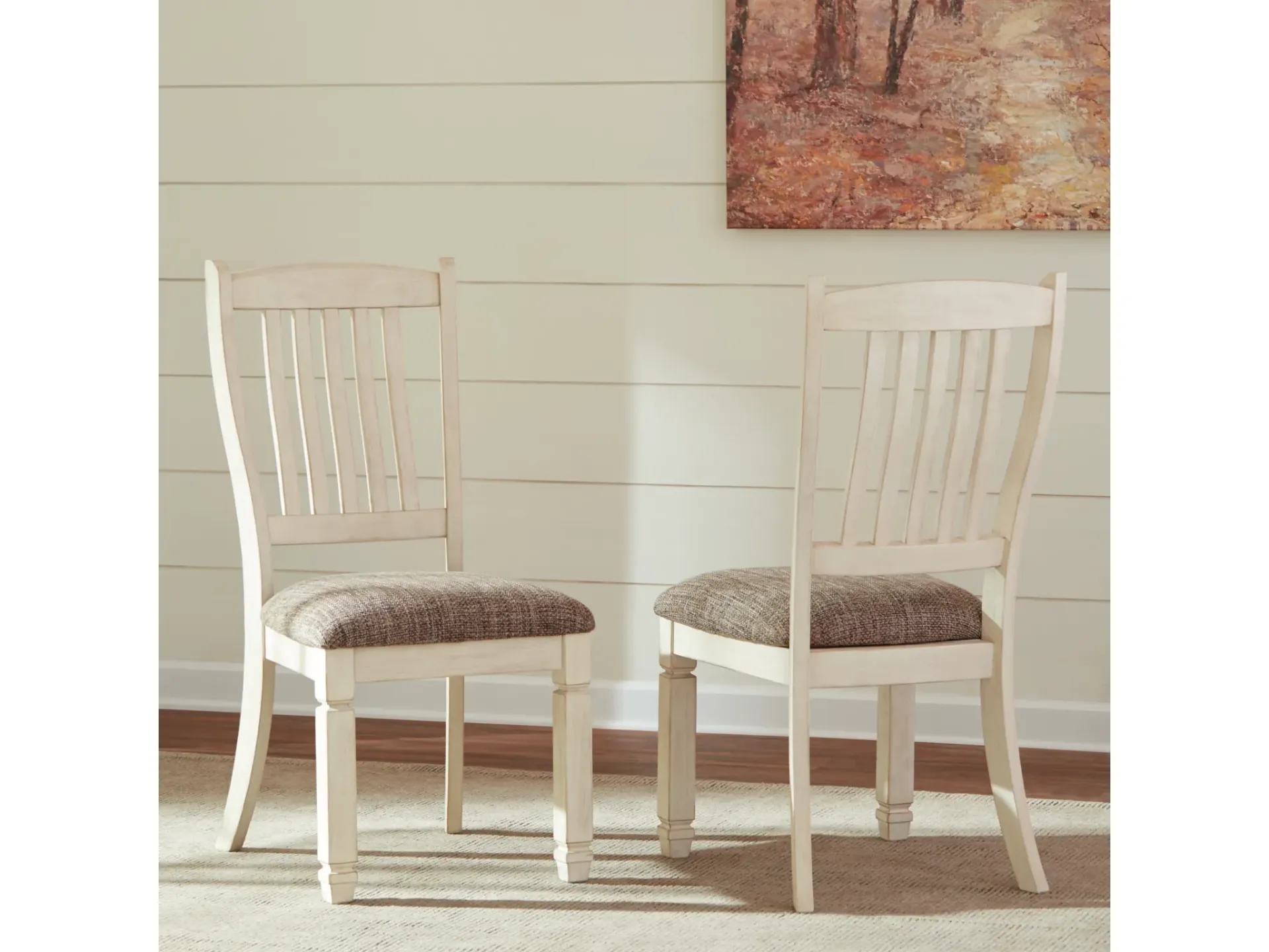 Two white chairs are sitting next to each other in a room with a painting on the wall.