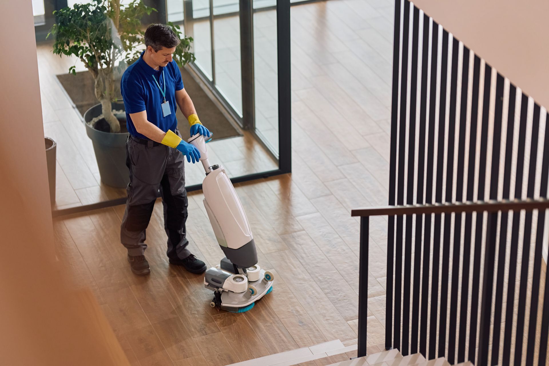 A janitor is using a professional floor scrubbing machine while cleaning the corporate office lobby.