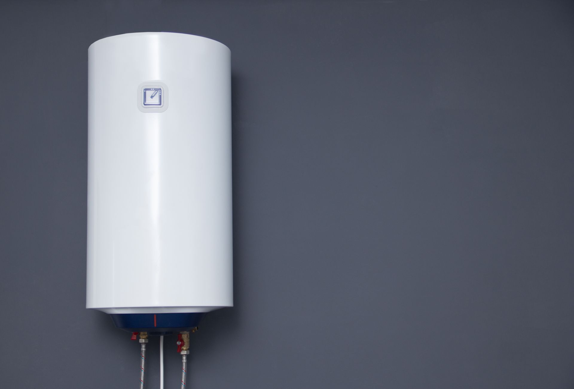 White cylindrical water heater on a gray wall with pipes below