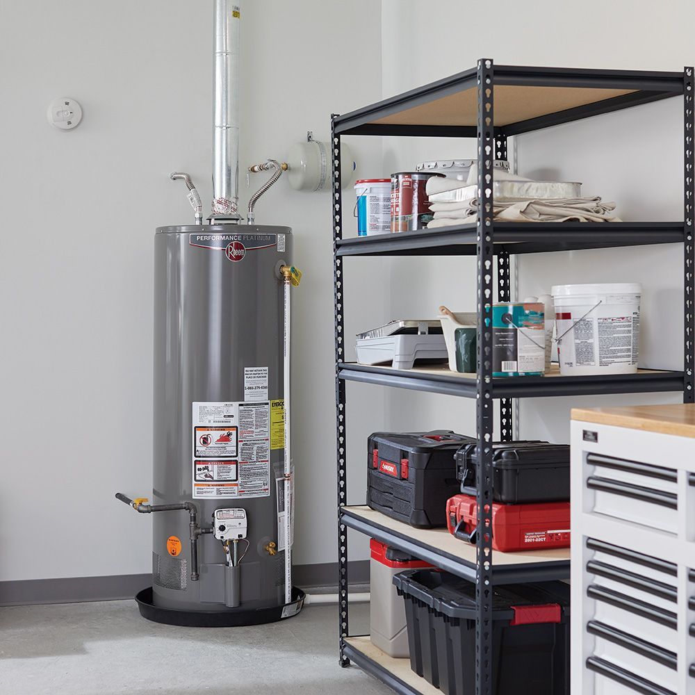 Gray water heater next to black shelving filled with supplies in a garage.