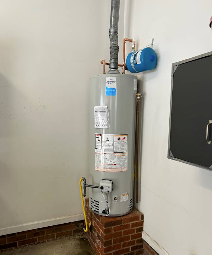 A water heater is sitting on top of a brick wall in a room.