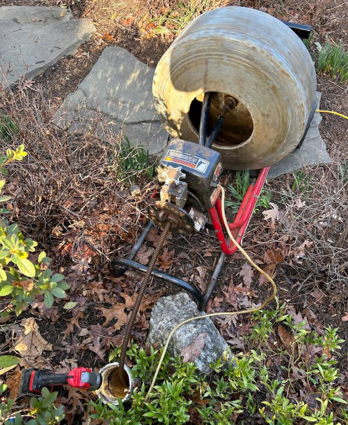 A drain cleaner is sitting on the ground next to a rock.