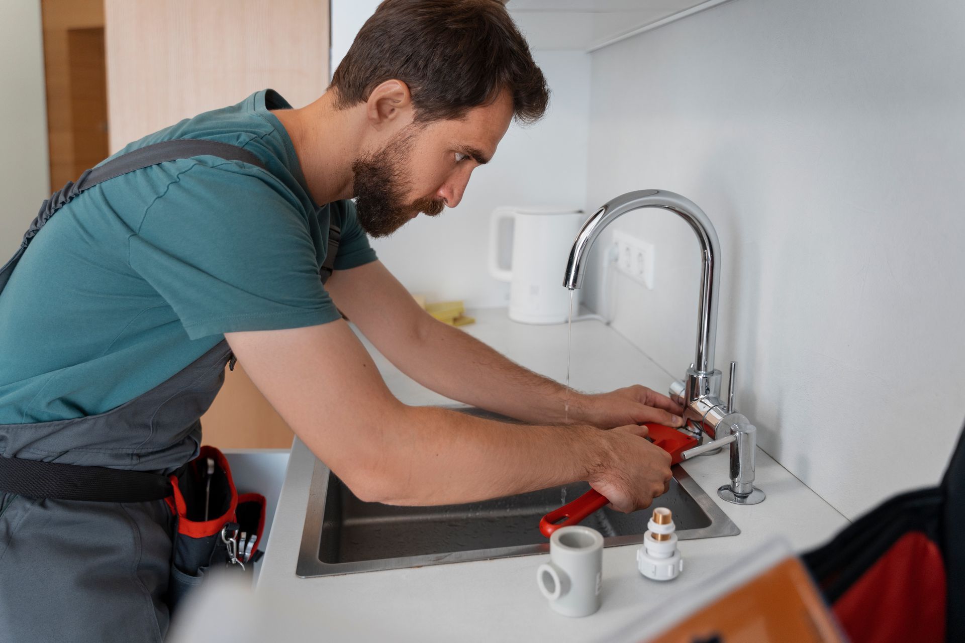 Plumber repairing a kitchen sink faucet with tools, leaning over the counter in a bright kitchen.