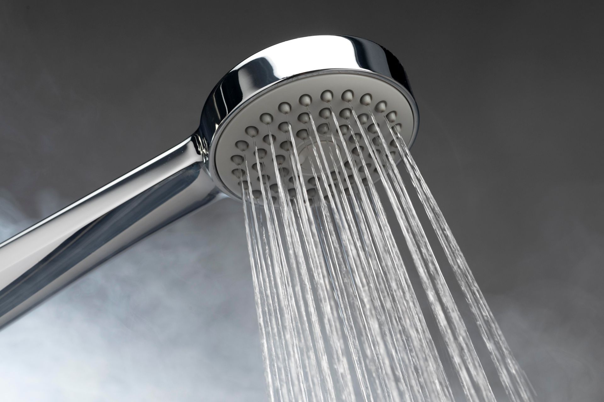 Chrome shower head spraying water, gray background.