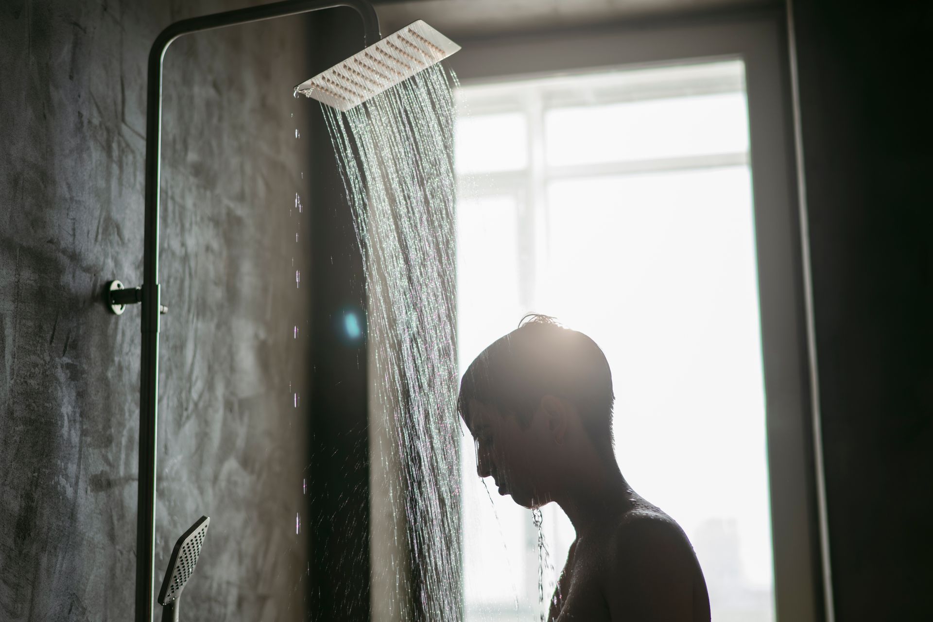 Person standing in a shower, water pouring down. Sunlight streams through a window.