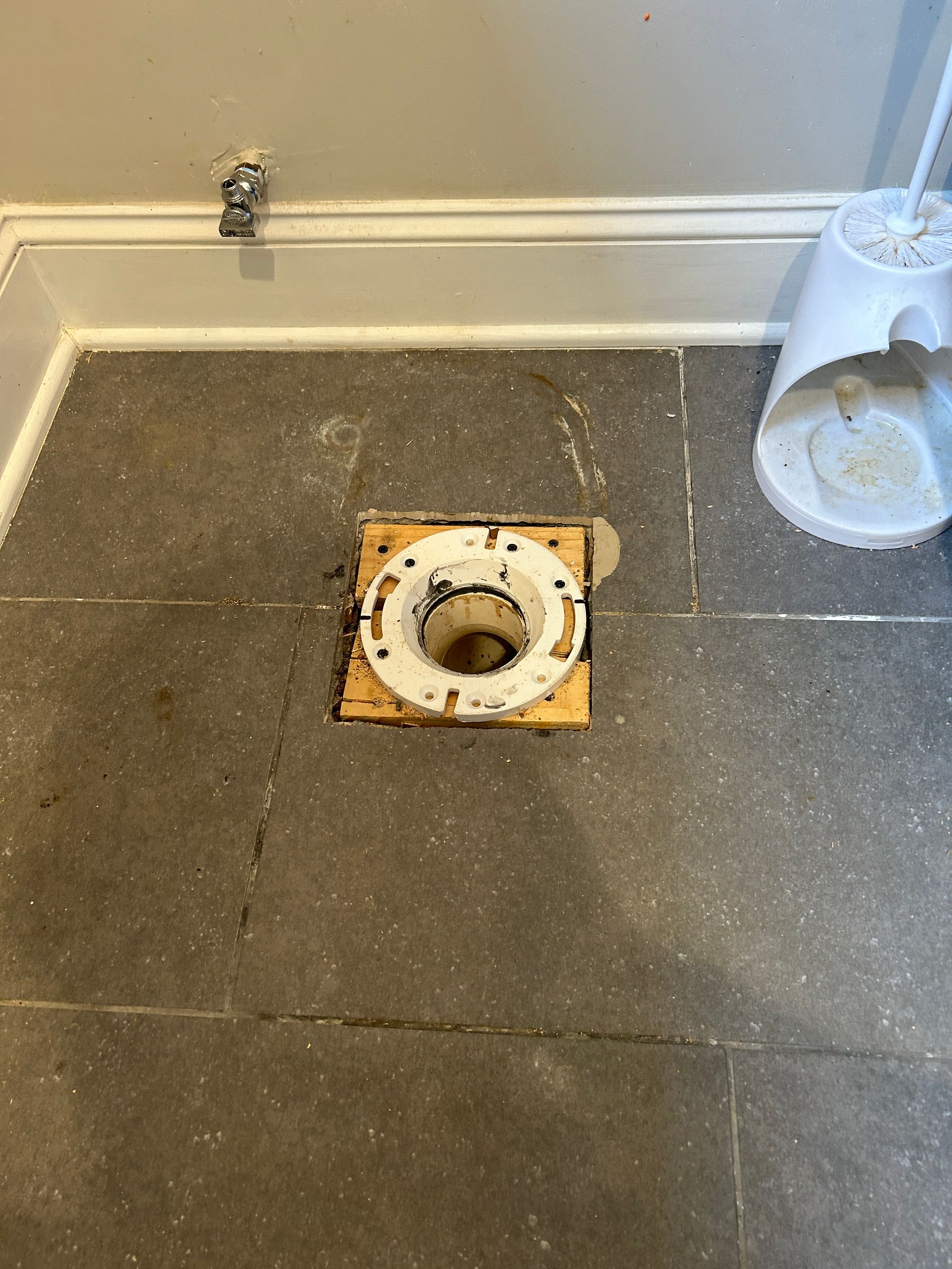 A hole in the floor of a bathroom next to a toilet.