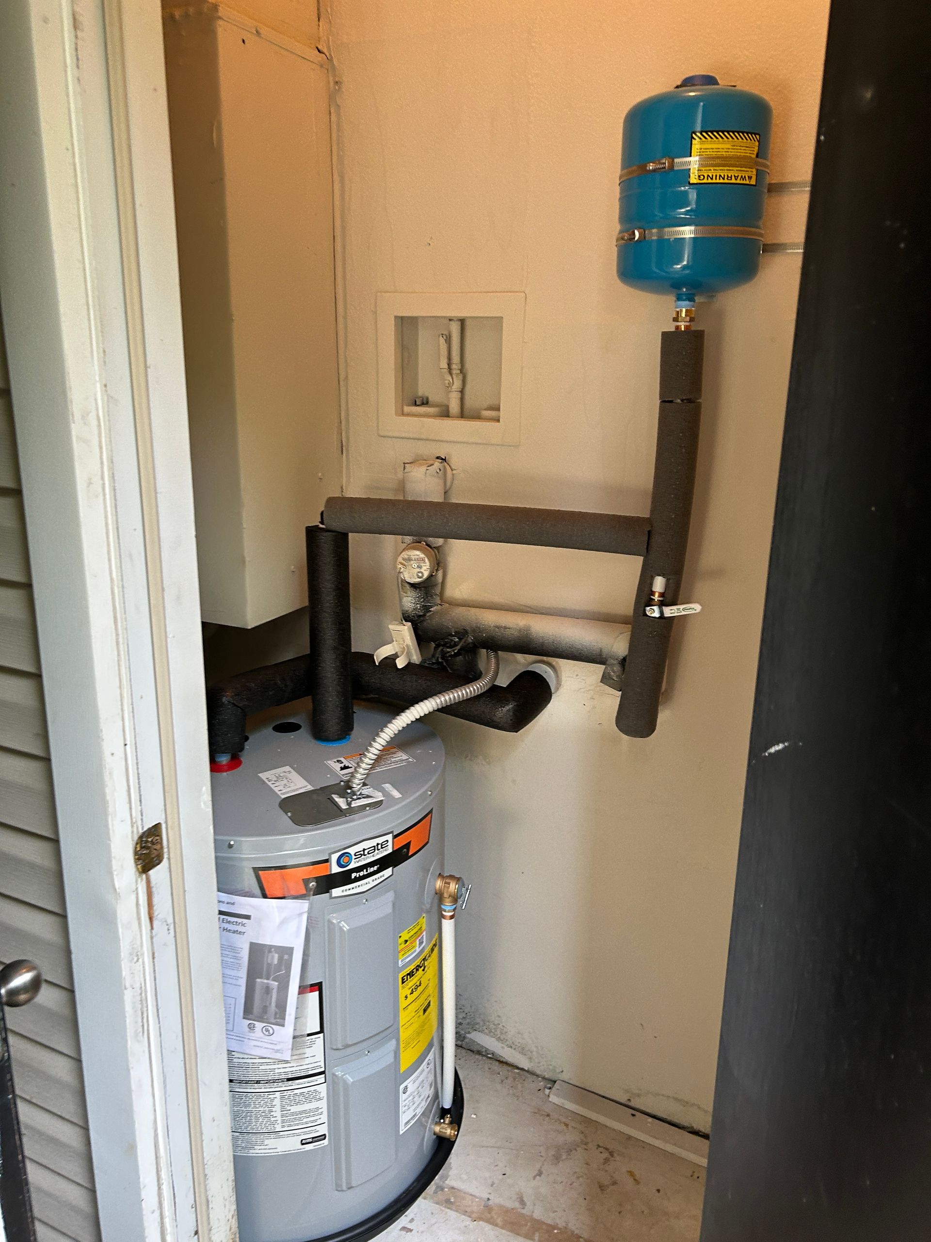 A water heater is sitting in a corner of a room next to a door.