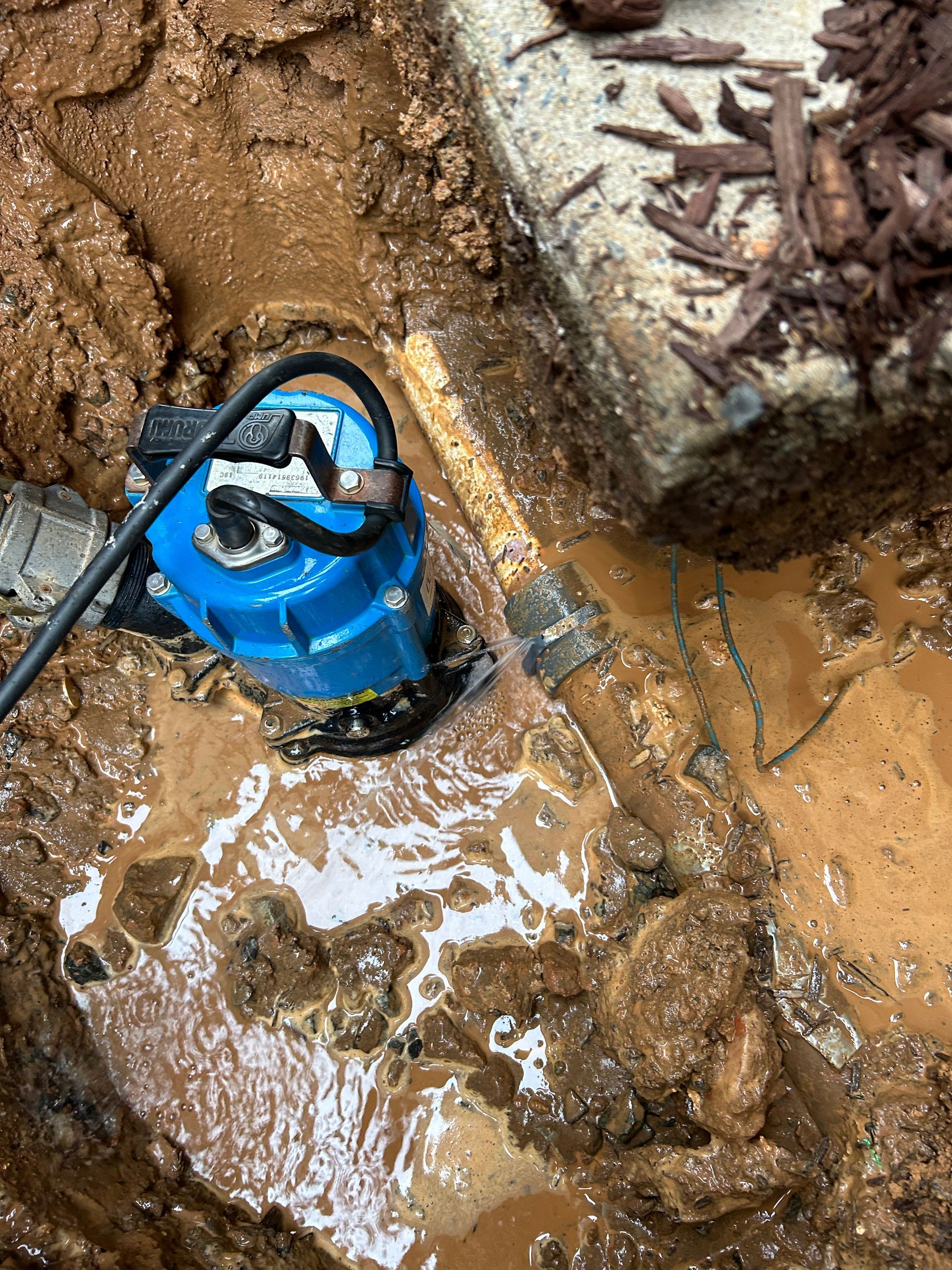 A blue pump is sitting in the mud next to a concrete block.