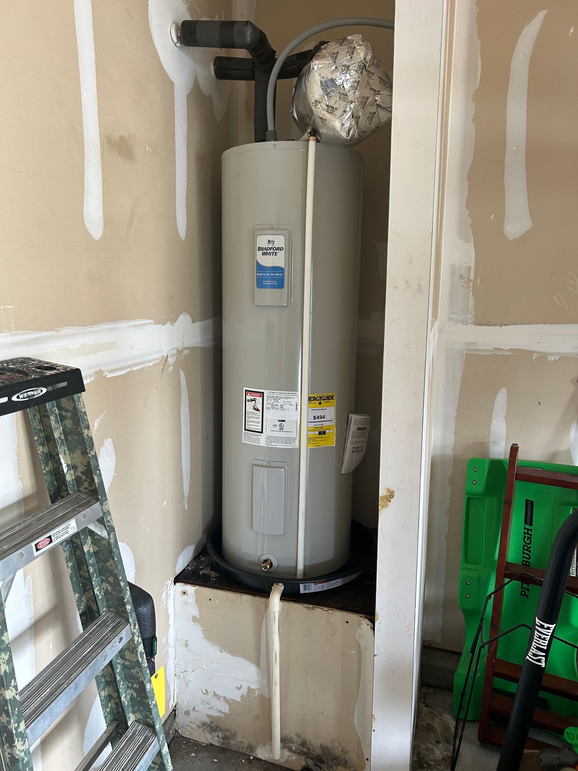 A water heater is sitting in a corner of a room next to a ladder.