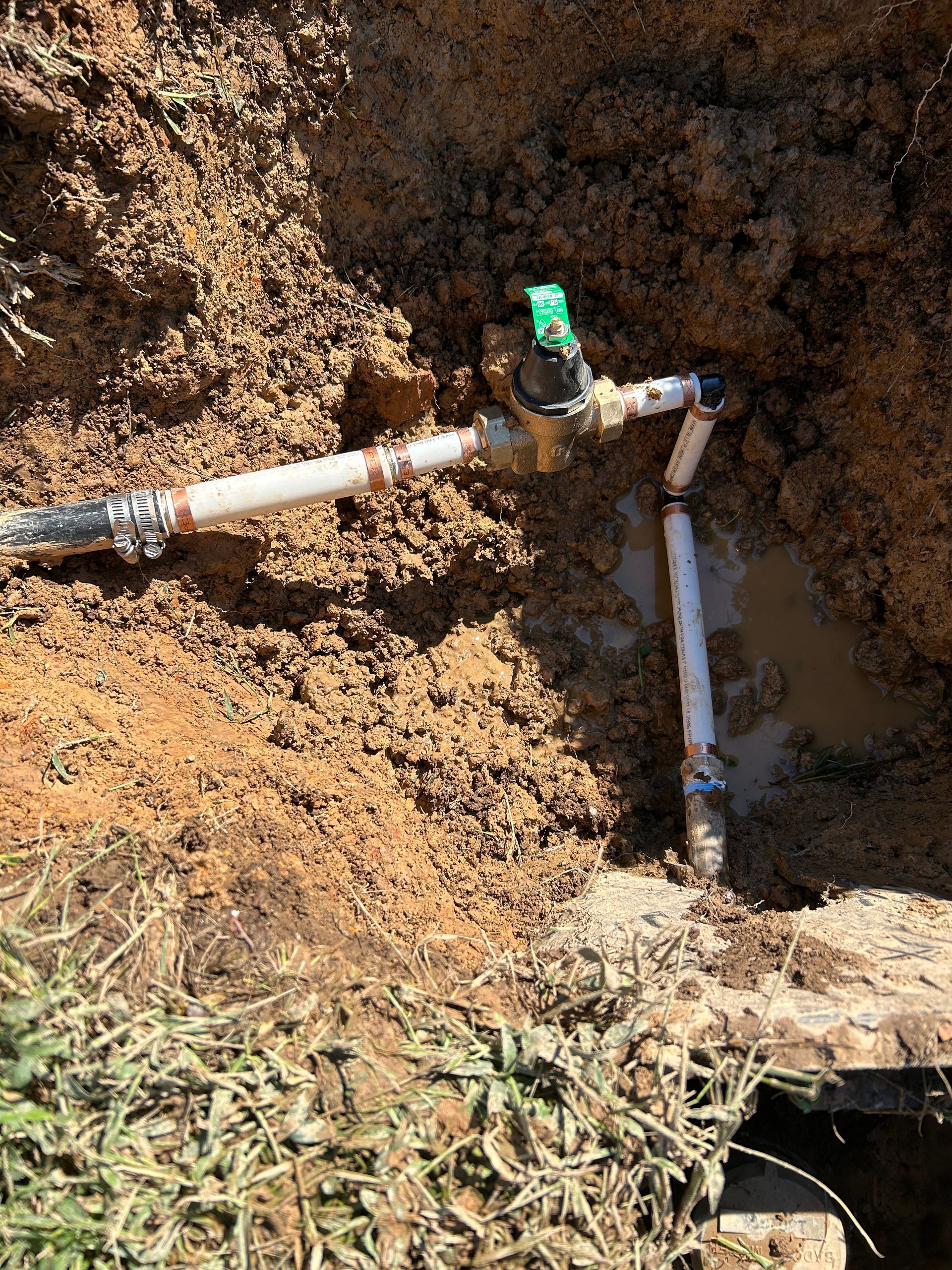 A water valve is sitting in the dirt next to a pipe.