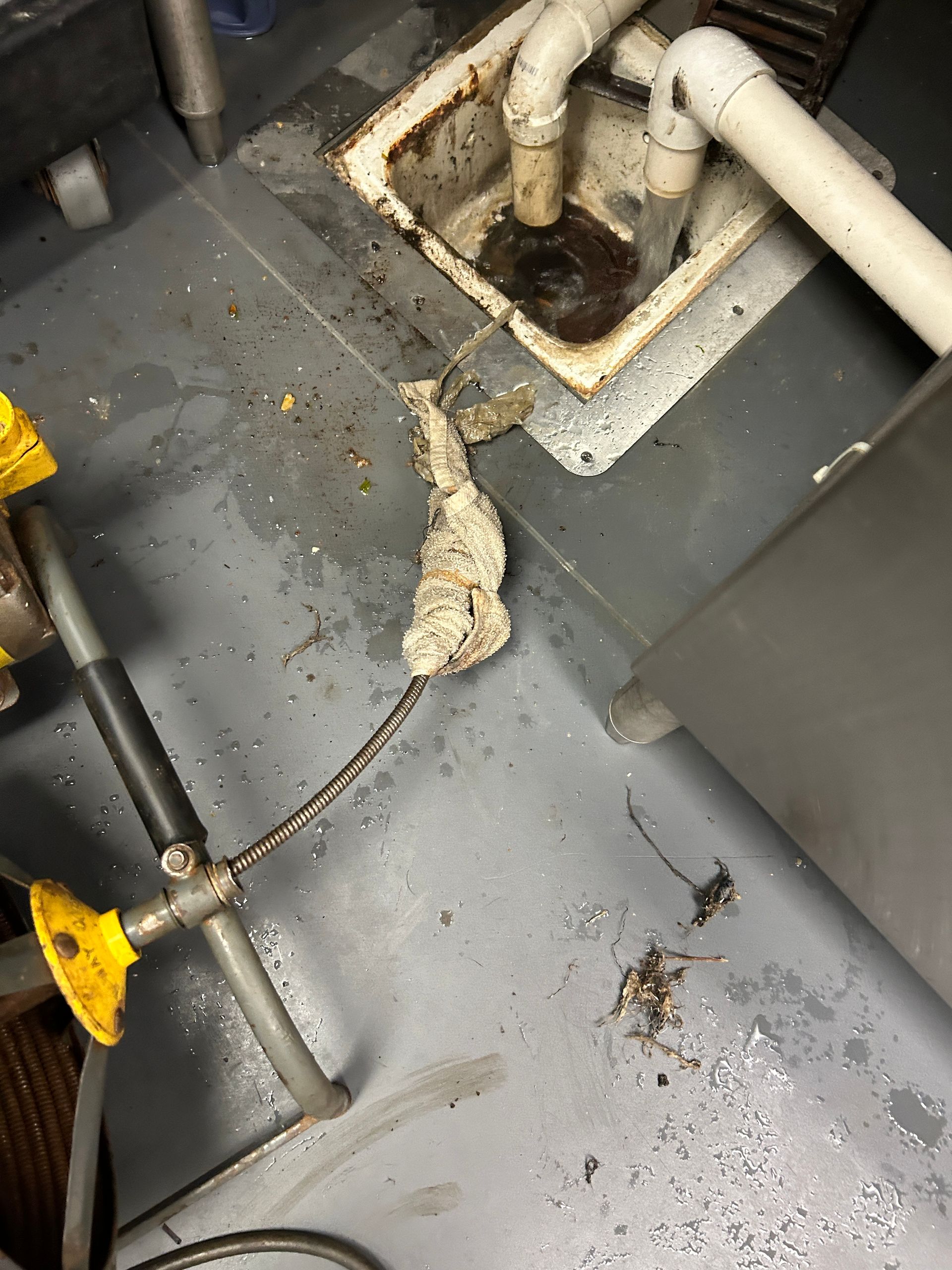 A dirty kitchen floor with a sink and pipes.