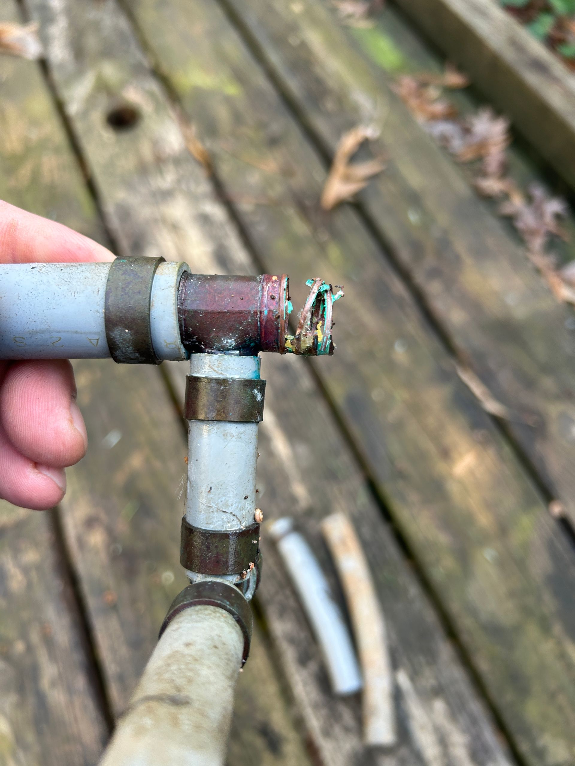 A person is holding a broken pipe on a wooden deck.