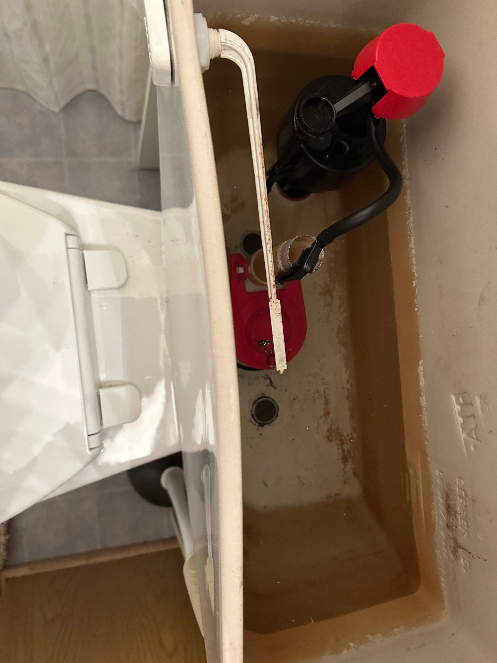 A close up of a toilet tank with a red valve