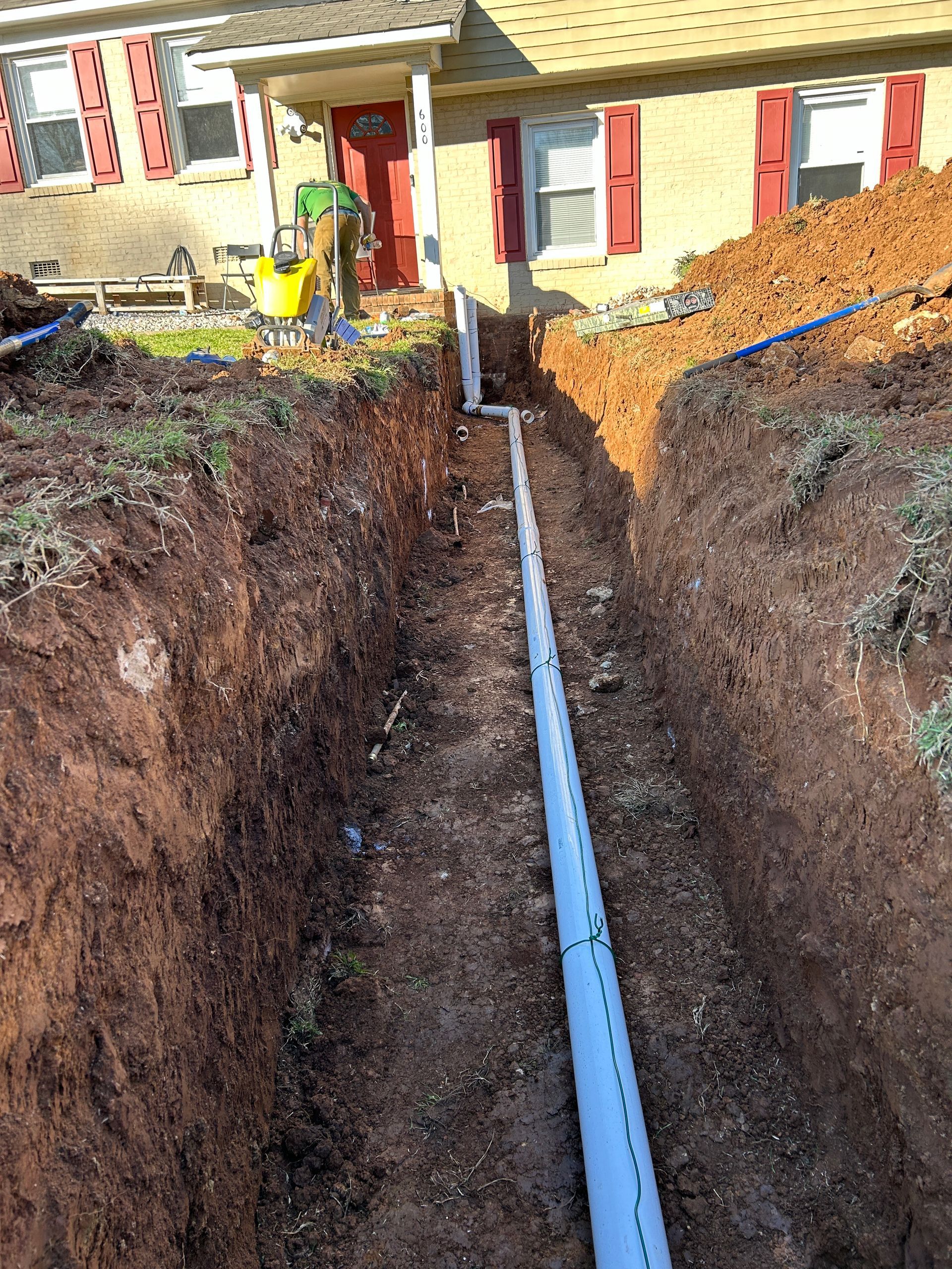 A drain pipe is being installed in the dirt in front of a house.