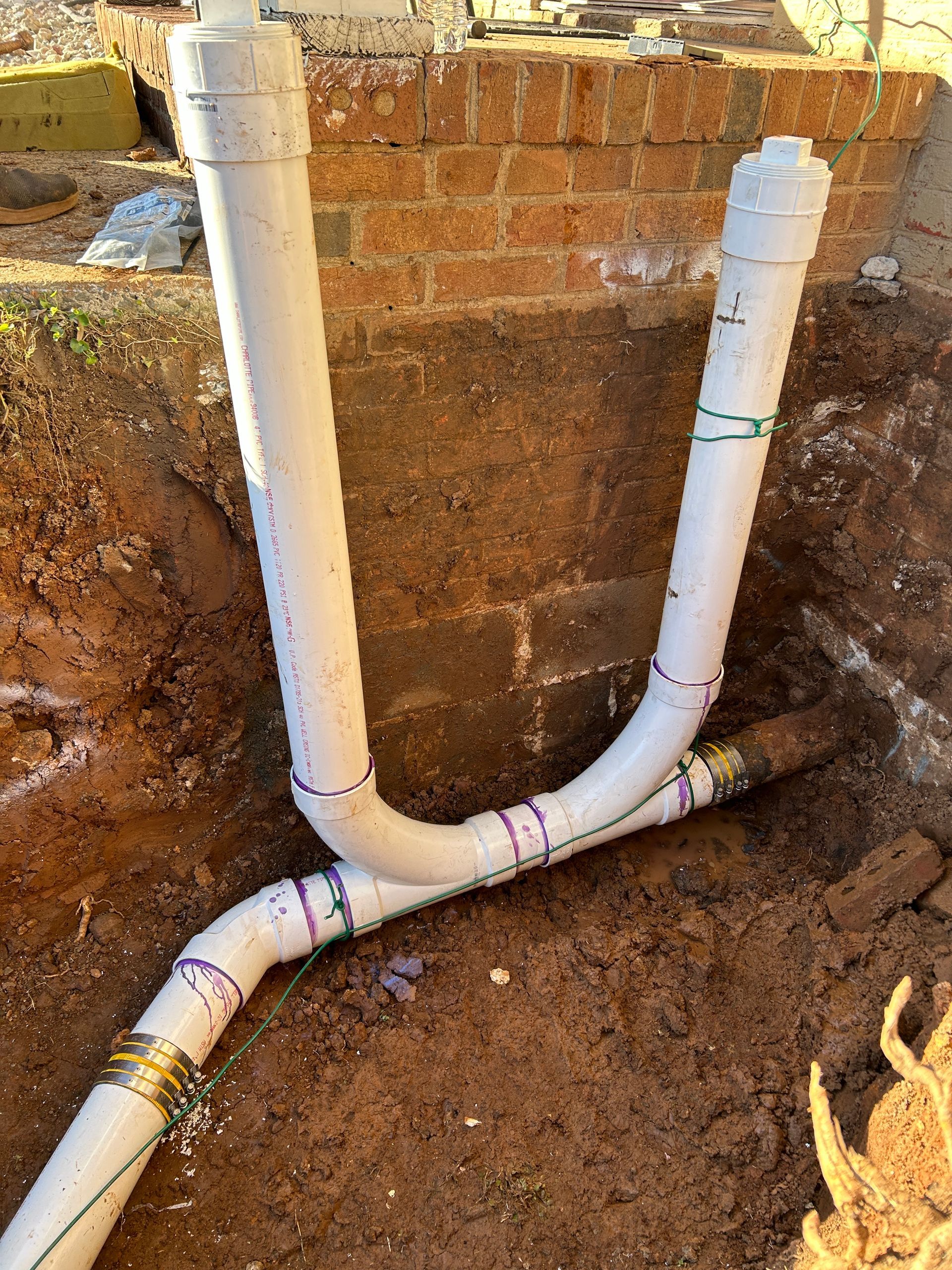A couple of white pipes sitting in the dirt next to a brick wall.