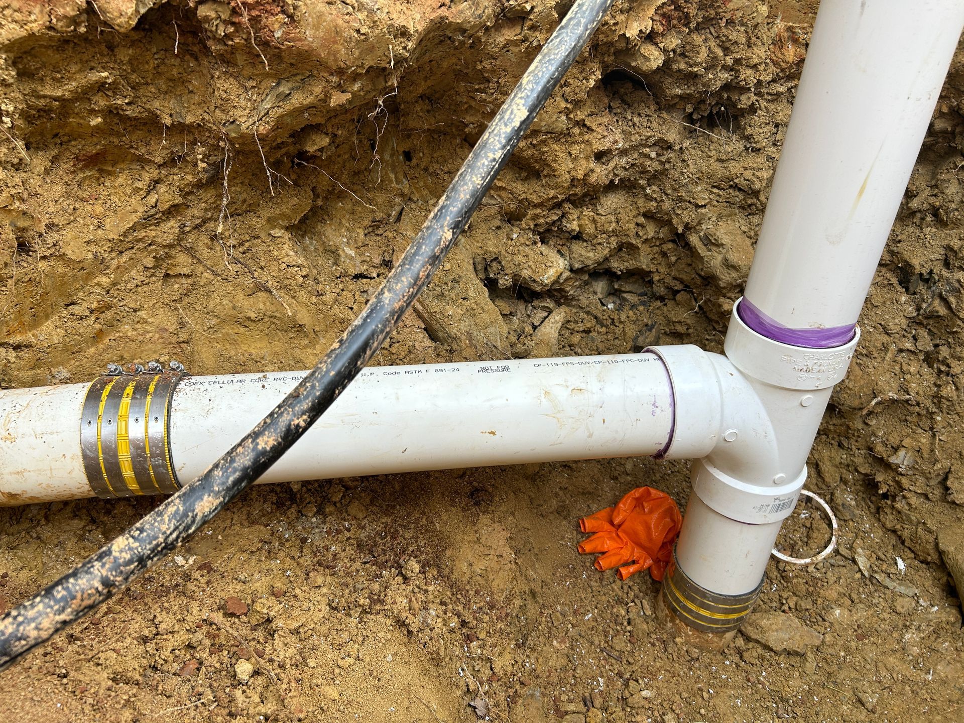 A white pipe is sitting in the dirt next to a wire.