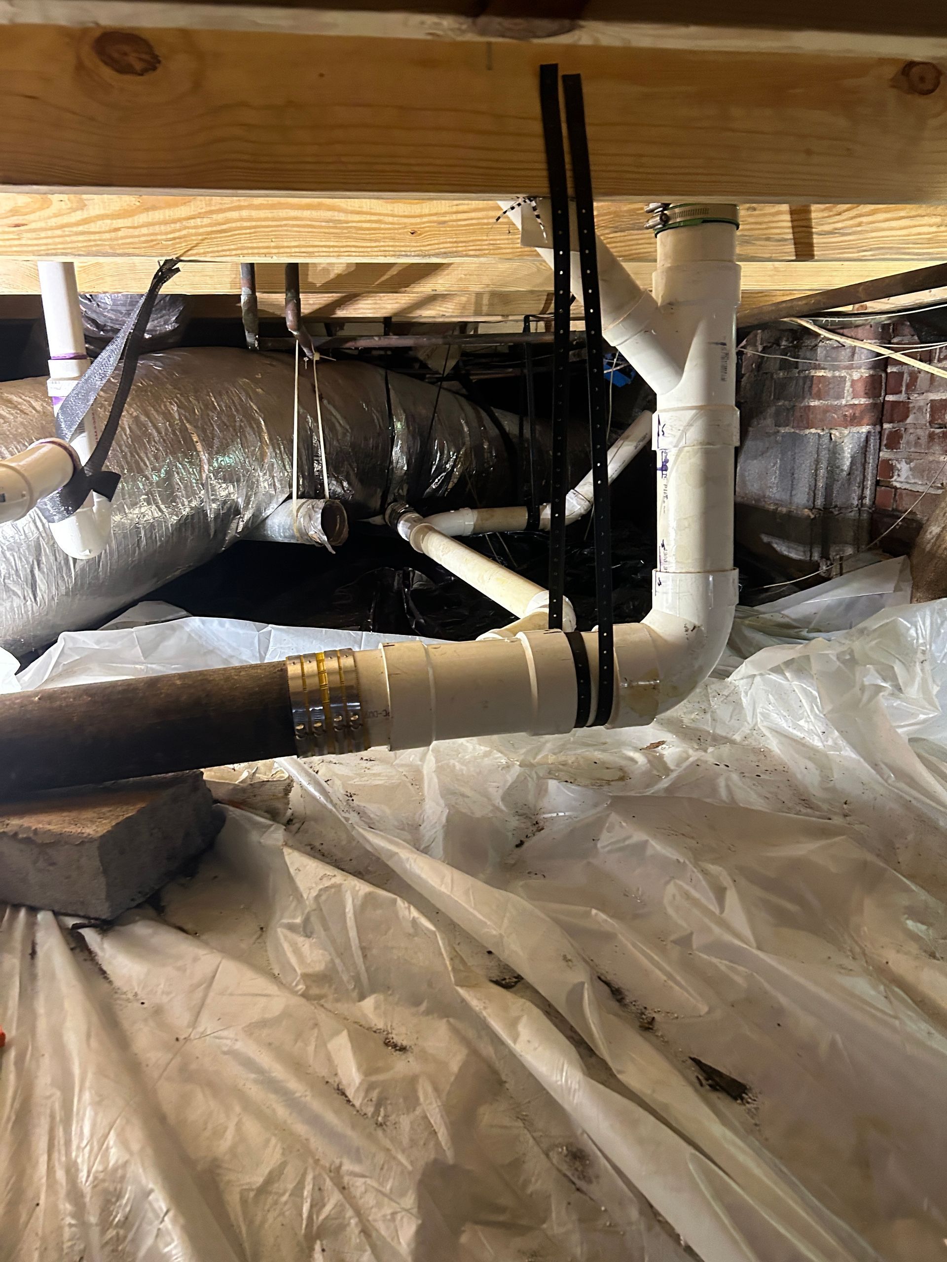 A bunch of pipes are under a wooden floor in a basement.