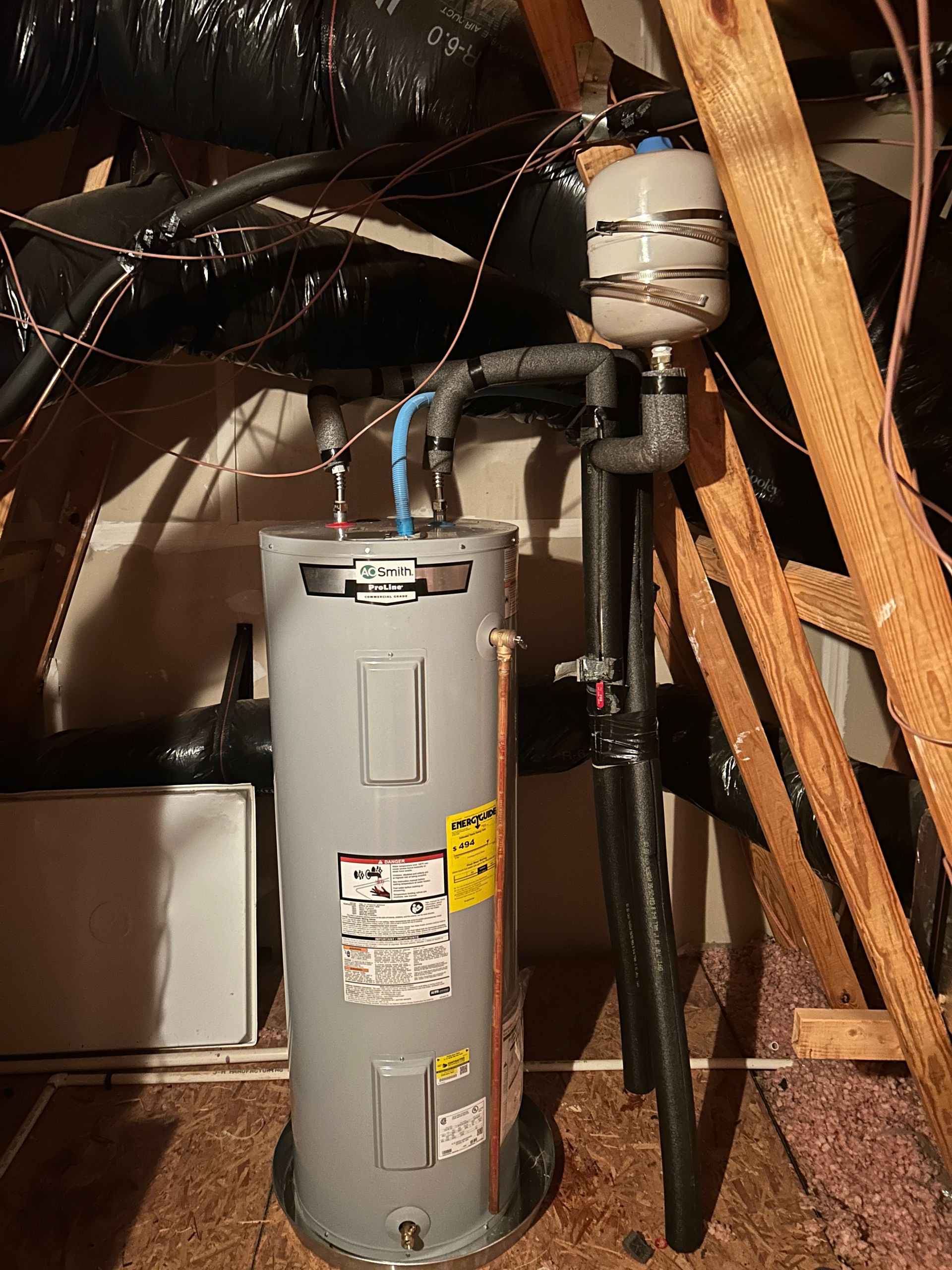 A water heater is sitting in a basement next to a wooden ladder.