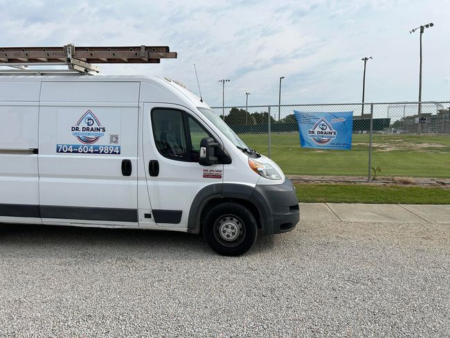 A white van is parked in a gravel lot in front of a field.