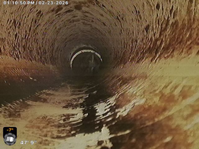 A man is kneeling down in front of a manhole cover with a camera attached to it.