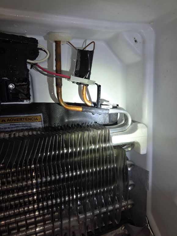 Close-up of the interior cooling coils and copper tubing inside a refrigerator, showing signs of moisture and ice.