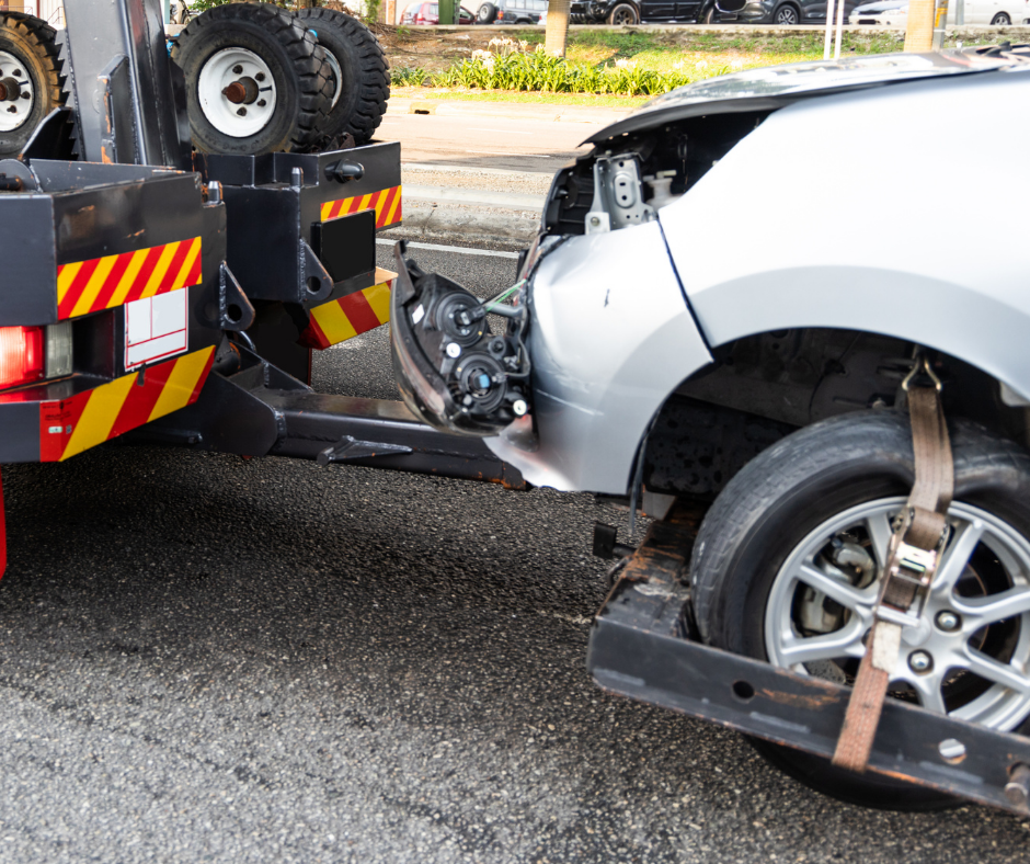 A silver car is being towed by a tow truck.