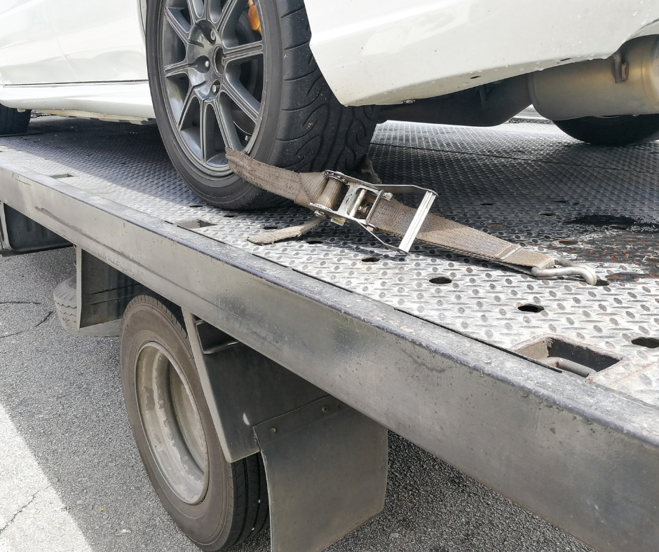 A white car is being towed by a tow truck.