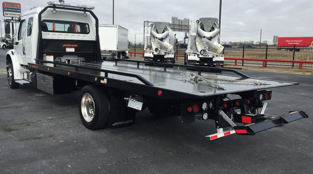 A tow truck with a flat bed is parked in a parking lot.