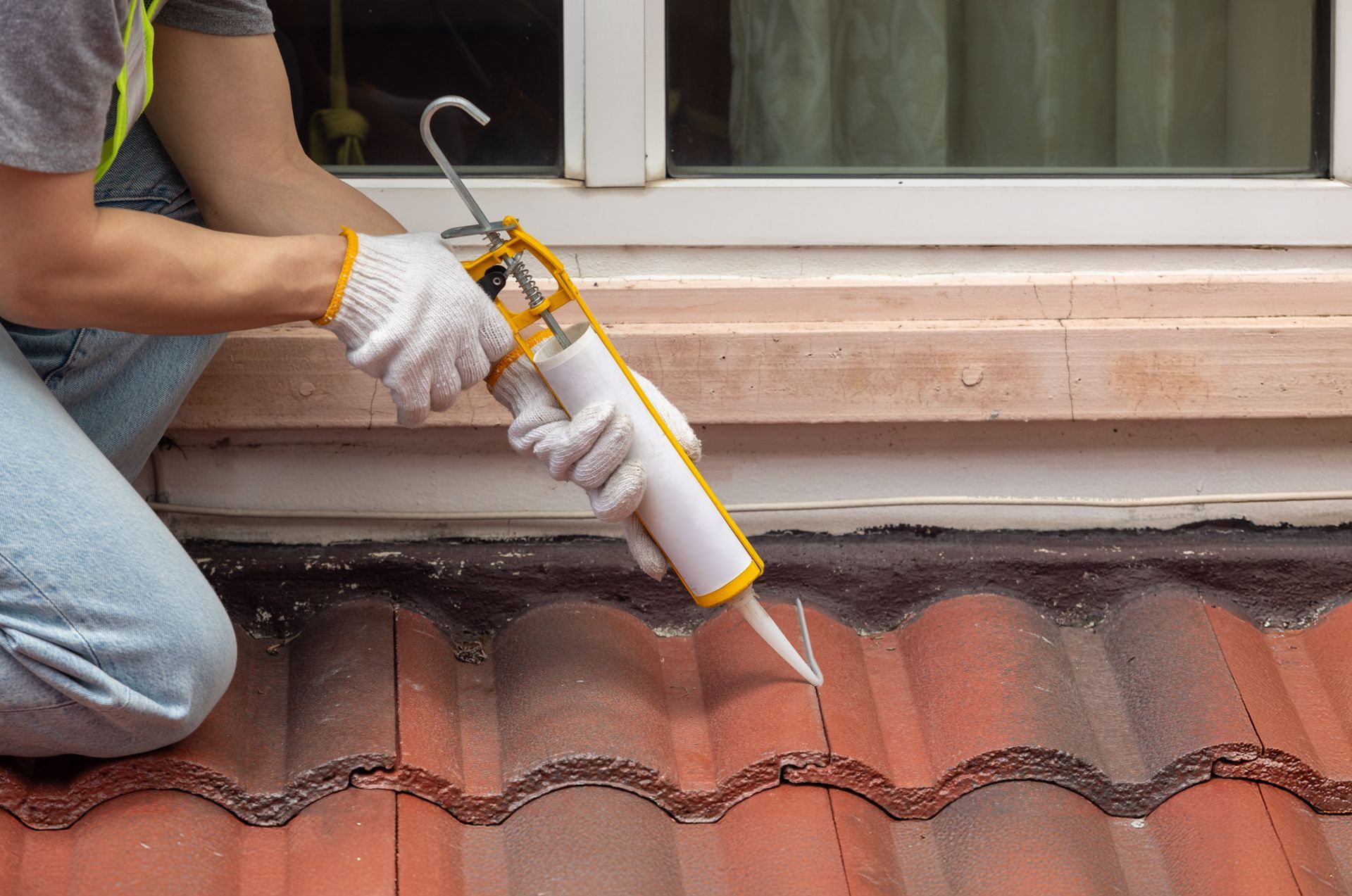 Worker applying sealant to roof seam with a caulking gun