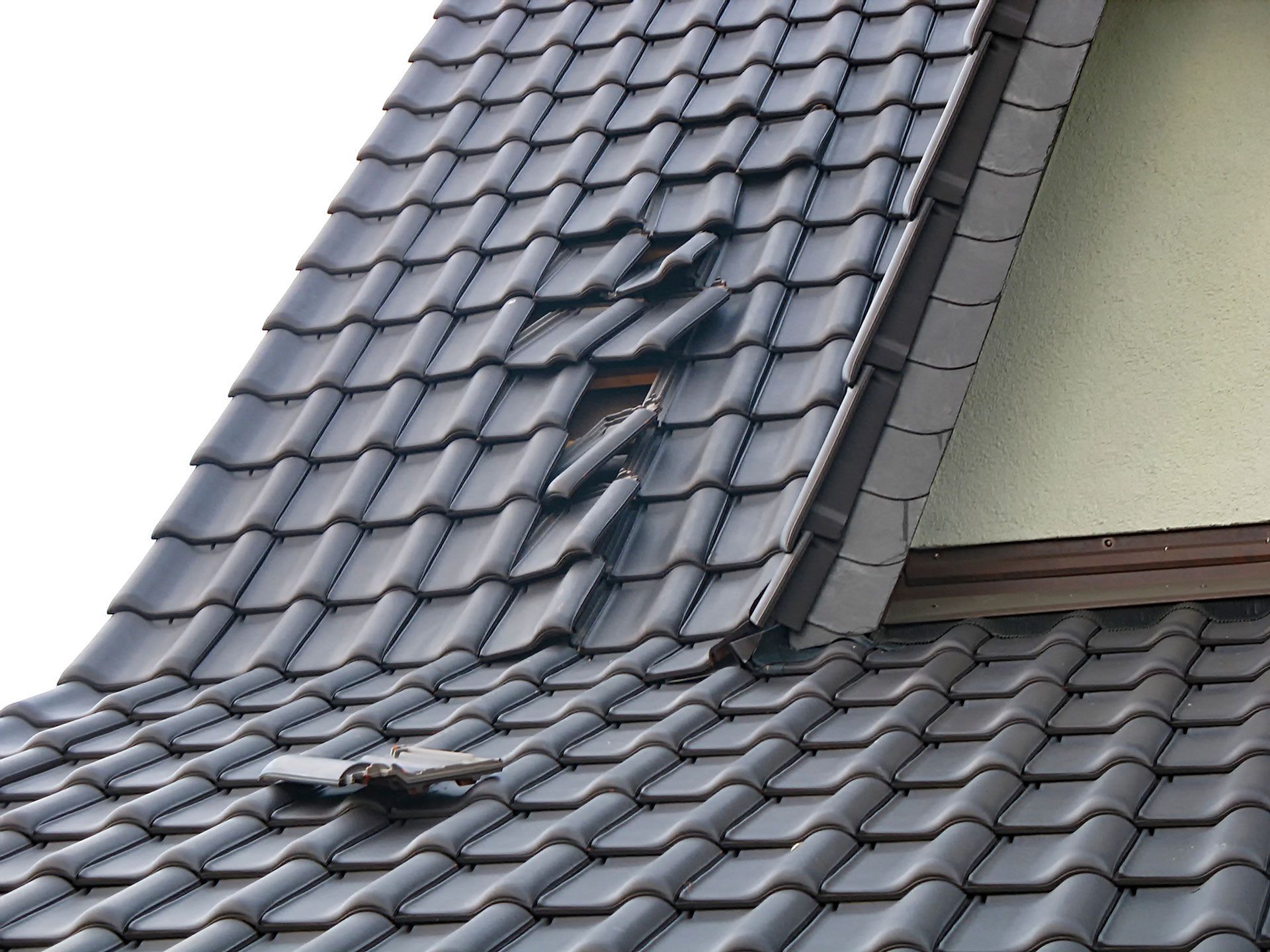 Dark gray tiled roof with a broken section exposing the underlayment
